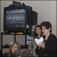 Audience asking questions with video conference on television in background
