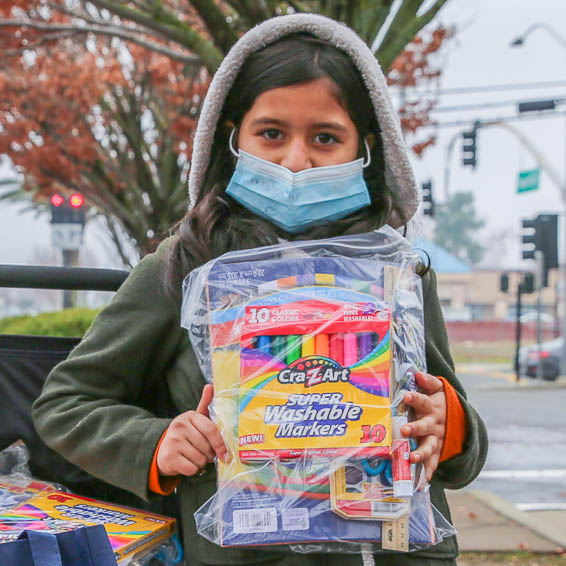 Young student standing on the sidewalk holding a bag of markers and art supplies