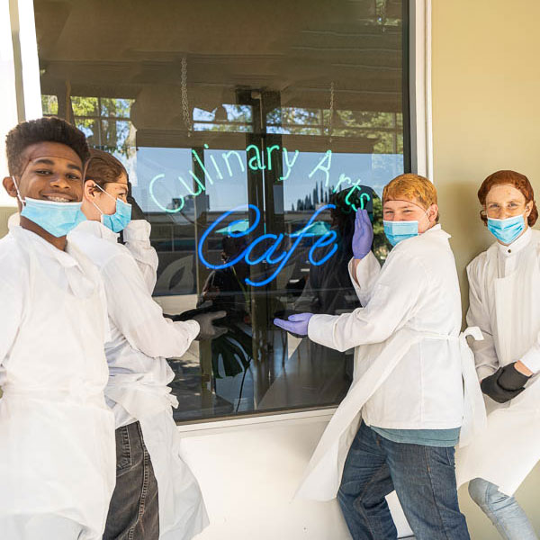 Students posing in front of the Culinary Cafe neon sign