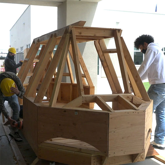 Students building a wooden play structure shaped like a helicopter