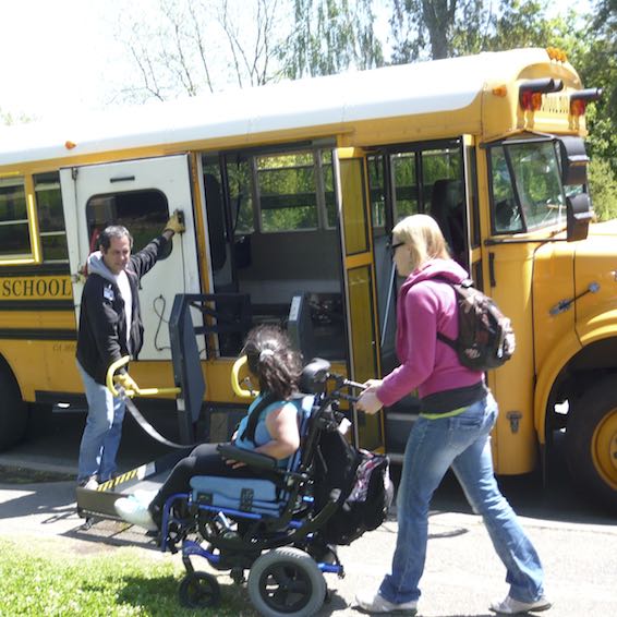 Student using wheelchair being helped onto school bus ramp