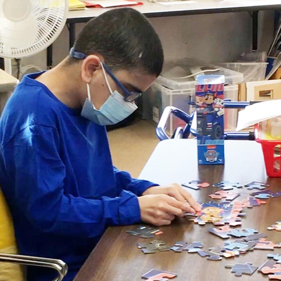 Mask-wearing student putting together a puzzle.