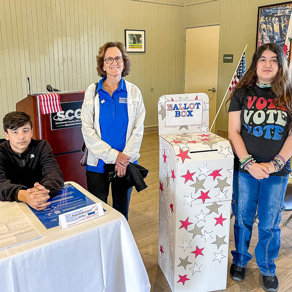 Bina Lefkovitz posing with students next to a cardboard ballot box