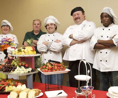 Culinary students, wearing chef hats, pose with trays of fruit