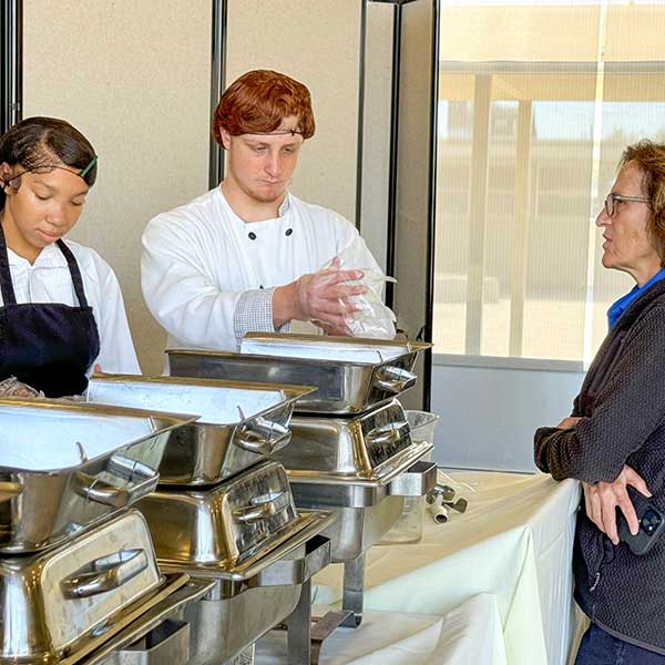 Students speaking to Board trustee while preparing to serve food