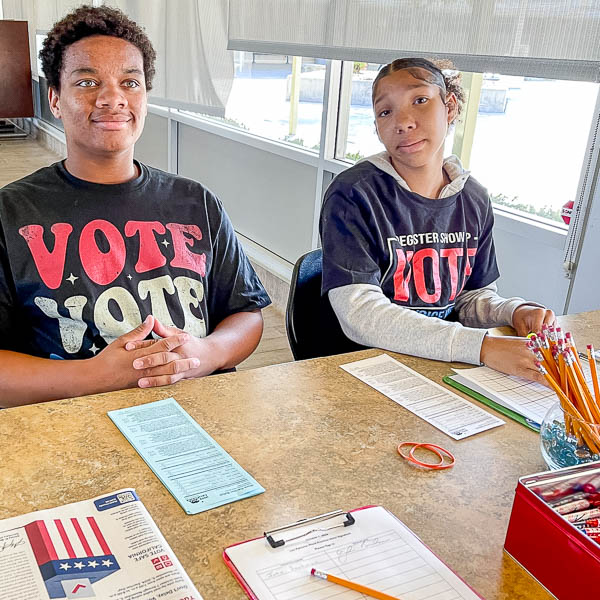 Seated students, wearing VOTE t-shirts, checking in voters