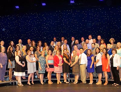 Large group of graduates posing on stage in front of starry background