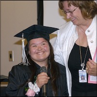 Staff member hugging graduate as she speaks into microphone