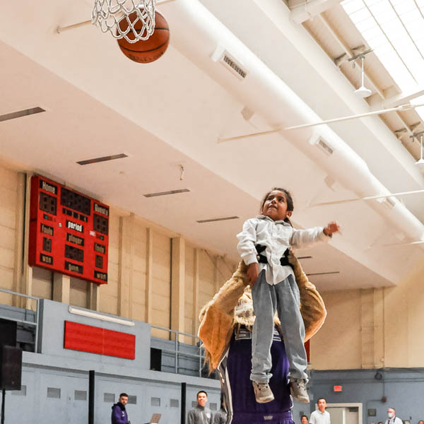Slamson lifting a student in the air to shoot a basket